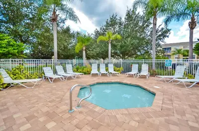 a swimming pool with chairs and a fence and palm trees at 8213 Fan Palm Way in Kissimmee