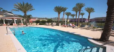 a swimming pool with palm trees and people sitting in chairs at 4 bedroom townhouse Sleeps 8 Coral Cay in Kissimmee