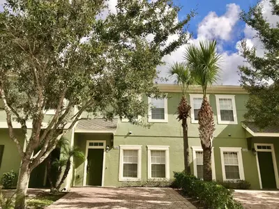 a green house with two palm trees in front of it at 4 bedroom townhouse Sleeps 8 Coral Cay in Kissimmee