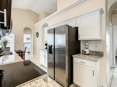 a kitchen with white cabinets and a stainless steel refrigerator at Family pool home near Disney wBBQ grill in Orlando