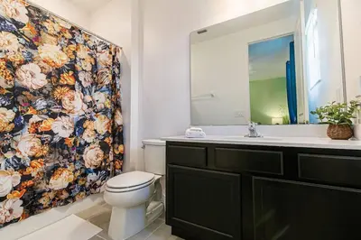 a bathroom with a toilet and a floral shower curtain at ☀️12BR Disney Villa Paradise w/ Game Room & Pool/Spa☀️ in Kissimmee