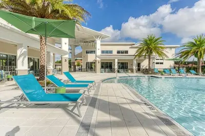 a swimming pool with blue lounge chairs and a green umbrella at ☀️12BR Disney Villa Paradise w/ Game Room & Pool/Spa☀️ in Kissimmee