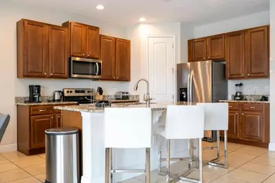 a kitchen with wooden cabinets and white bar stools at Unforgettable Experience Luxury Vacation Home 7479 in Orlando
