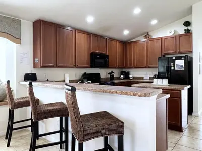 a kitchen with wooden cabinets and a counter with bar stools at Cozy 4 Bed 3 Bath Pool Hm with Game Room-4450NP in Kissimmee
