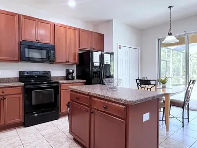 a kitchen with wooden cabinets and a table with a counter top at Beautiful 6Bd Pool Hm Veranda Palms-4464NP in Kissimmee