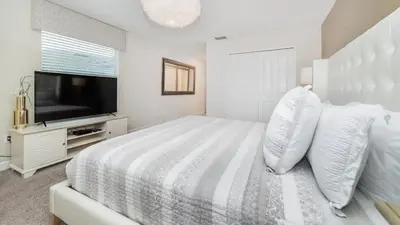 a white bedroom with a large bed and a flat screen tv at 4749 Kings Castle in Kissimmee