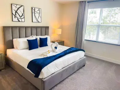 a bedroom with a large bed with blue pillows and a window at 3 bedrooms pool home Hidden Forest Resort Amenities in Orlando