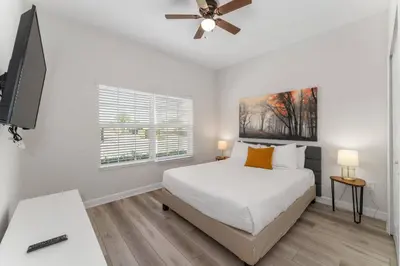 a white bedroom with a bed and a flat screen tv at Townhome with pool at Storey Lake in Kissimmee