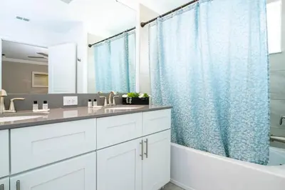 a bathroom with white cabinets and a blue shower curtain at Vibrant Themed Home Prime Location in Kissimmee