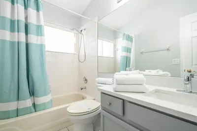 a white bathroom with a tub and a toilet and a sink at Magical 5-Bedroom Retreat w/ Pool, 3 Ensuite Bedrooms, Near Disney, and Internet! in Kissimmee