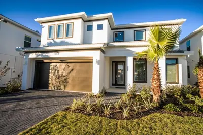 a white house with a garage and a palm tree at Gorgeous Vacation Home near Everywhere in Kissimmee