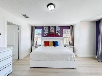 a white bedroom with a white bed with colorful pillows at Tranquility Hut, Spacious 4-bedrooms, 4-bathrooms, Pools, free parking in Kissimmee
