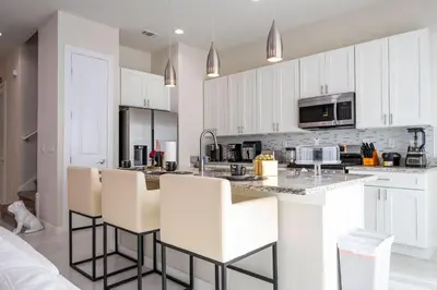 a kitchen with white cabinets and white bar stools at New Exclusive Villa 5 min to Disney in Orlando