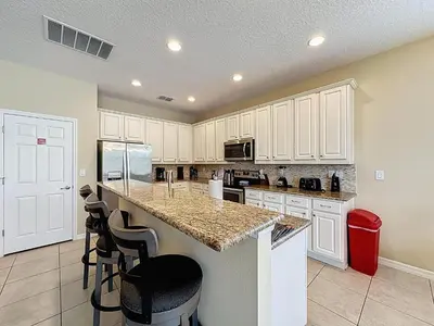 a kitchen with white cabinets and a counter with stools at Veranda Home, 8br, 6 en-suites, Lake View,POOL/SPA in Kissimmee