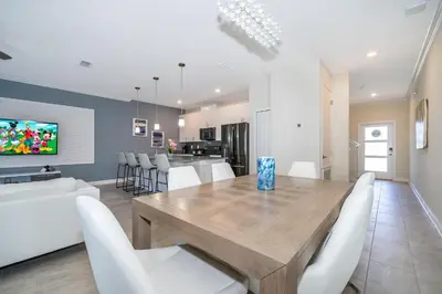a dining room and kitchen with a wooden table and white chairs at 2921DH TOWNHOUSE 4 BEDROOMS & 3 BATHROOMS + POOL in Kissimmee