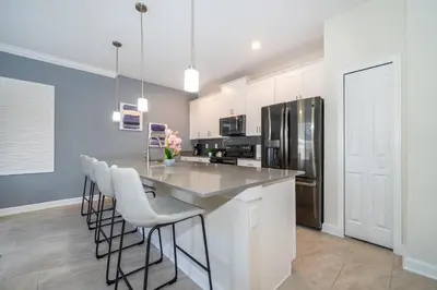 a kitchen with white cabinets and a large island with bar stools at 2921DH TOWNHOUSE 4 BEDROOMS & 3 BATHROOMS + POOL in Kissimmee