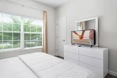 a white bedroom with a bed and a tv on a dresser at Really close to Disney! Sleeps 10 - STL116 in Kissimmee