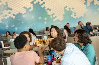 a group of people sitting at a table eating pizza at Universal's Stella Nova Resort in Orlando