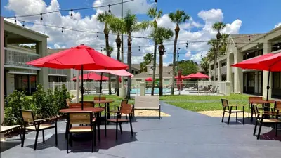 a patio with tables and chairs with red umbrellas at Pool - WiFi - Parking - Best Location ! in Kissimmee