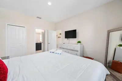 a white bedroom with a large white bed and a tv at Magic Marvel Getaway in Kissimmee