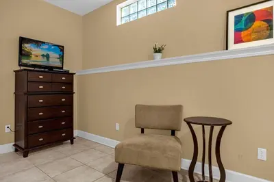 a living room with a chair and a dresser at Sunny Summer Awaits - Renovated Townhome by Disney! in Orlando