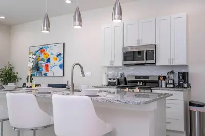 a kitchen with white cabinets and a counter with white chairs at Amazing 2024 Villa 5 min to Disney in Orlando