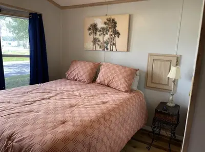 a bedroom with a bed with a pink comforter and a window at Sherwood Forest Mobile Home in Kissimmee