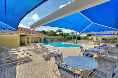 a pool with chairs and tables and blue umbrellas at Allure - Sleeps 8 - 3 BDM - Disney in Kissimmee