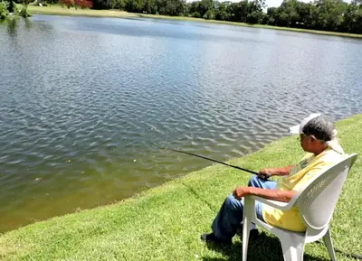an older man sitting in a chair fishing in a lake at 1061 Lake Berkley 4 Bed with Pool in Kissimmee