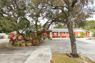 an orange building with trees and flowers in a parking lot at Banana Leaf Villa-Vintage Vibes Suites in Orlando