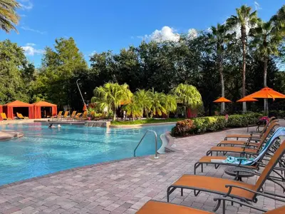 a large swimming pool with chairs and umbrellas at Grand Deluxe 3BR Townhouse near Disney Parks in Kissimmee