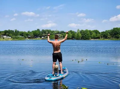 a man standing on a paddle board with a dog at Spring-Fed Lake King Suite Pet Friendly in Orlando