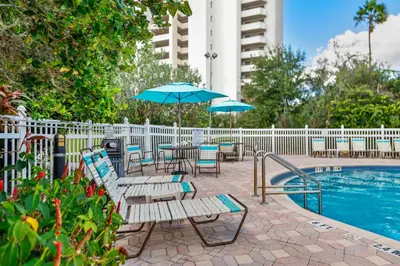 a pool with chairs and tables and umbrellas next to a building at 2 Suites at The Enclave Near Universal in Orlando