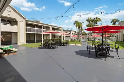 a patio with tables and chairs with red umbrellas at 11 Condo-Hotel With Double Bed And Community Pool Miles From Disney! in Kissimmee