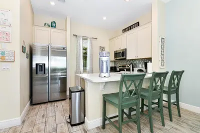 a kitchen with a counter and chairs and a refrigerator at Seashell Cream Cottage With Private Pool Near Disney With Margaritaville Resort & Island H2O Access - 8037St in Orlando
