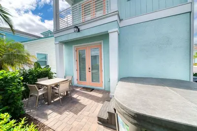 a patio with a table and chairs in front of a blue house at Sail Away! Beautiful Cottage With Private Hot Tub Near Disney With Margaritaville Resort & Island H2O Access - 3045Sp in Orlando