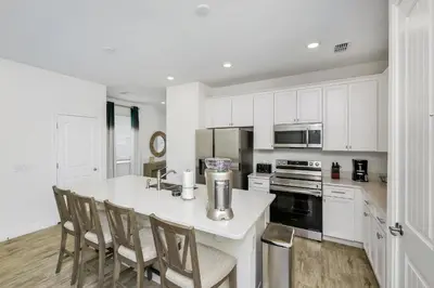 a kitchen with white cabinets and a kitchen island with chairs at Beautiful Waterfront Villa Near Disney With Margaritaville Resort & Island H20 Waterpark Access - 3017Cs in Orlando