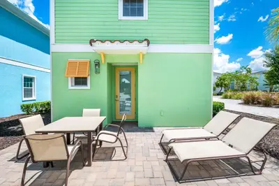 a patio with tables and chairs in front of a green house at Luxurious Cottage Near Disney With Margaritaville Resort & Island H2O Access - 8000Dr in Orlando