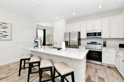 a kitchen with white cabinets and a counter with stools at Sunny Villa Near Disney With Margaritaville Resort & Island H20 Access - 8151Cp in Orlando