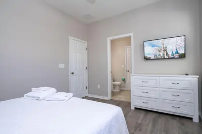 a white bedroom with a bed and a tv on the wall at 4BR Lakefront - Themed Rooms - Pool & BBQ! in Kissimmee