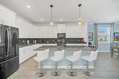 a large kitchen with white cabinets and white stools at Spotless 6 bedroom Villa - Storey Lake - Hot tub - Free Water Park - 15 Mins to Disney in Kissimmee