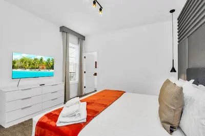 a white bedroom with a bed and a tv at 5BR Family Haven Near Disney with Private Pool in Kissimmee