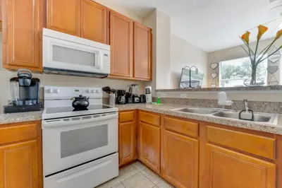 a kitchen with white appliances and wooden cabinets at 4 Mi to Disney! Family Townhome with Pool Access in Kissimmee