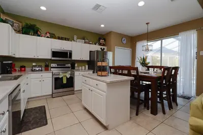 a kitchen with white cabinets and a dining room with a table at Spacious Emerald Island Resort Home with Pool Spa and Resort Amenities near Disney in Kissimmee