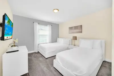 a white bedroom with two beds and a flat screen tv at 4829Lullaby townhouse in Kissimmee