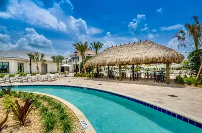 a resort swimming pool with chairs and a thatch roof at 4741Clock Unit208 townhouse in Kissimmee