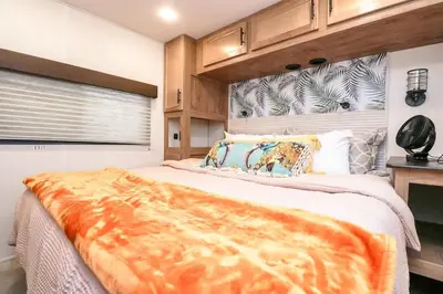 a bedroom with a large bed with an orange blanket on it at FunTropicalTinyHomeGolfCartLake in Orlando