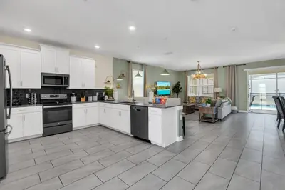 a large kitchen with white cabinets and a living room at Storey Lake Dream Villa with Private Pool in Kissimmee