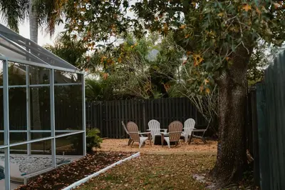 a patio with chairs and a tree next to a fence at Luxury Private Pool Villa near Disney with Fire Pit, Game Room & More in Kissimmee