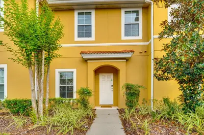 a yellow house with a white door and trees at 4 Mi to Disney World Townhome with Hot Tub and Lanai! in Kissimmee